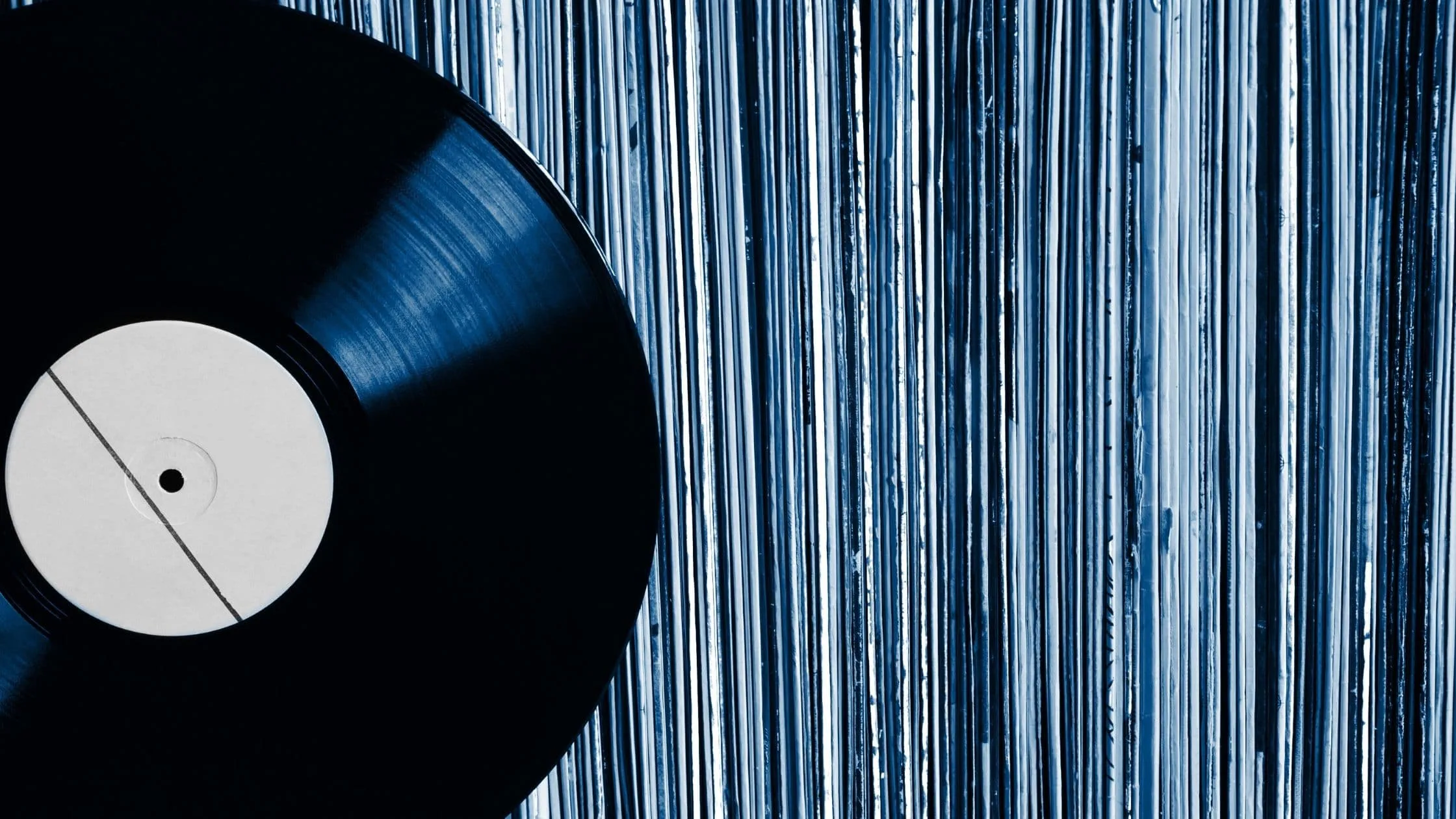 Hands pulling a vinyl record from its sleeve at a record store counter with a turntable nearby